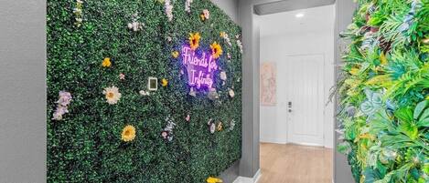Un pasillo con una pared verde cubierta de follaje y un letrero de neón que dice 'Friends for Infinity'.