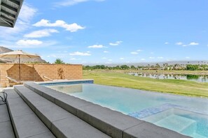 A swimming pool with steps leading down to the water, a grassy area, and a distant view of a city skyline.