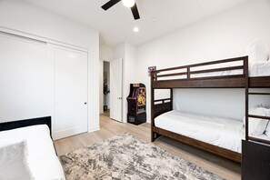A bedroom with bunk beds, a door, a small arcade machine, and a patterned rug.