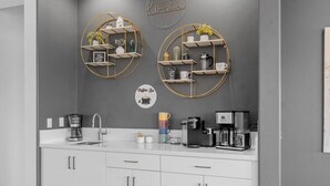 Una cocina moderna con armarios blancos, un espacio para café y dos estantes empotrados con objetos decorativos.