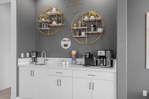 Una cocina moderna con armarios blancos, un espacio para café y dos estantes empotrados con objetos decorativos.