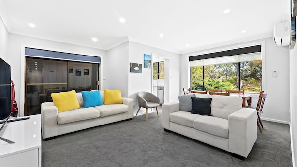 A modern living room with two sofas, a dining area, and a view of the outdoors. - Apollo Unit 1 - Ground Floor - A Block (Narooma)
