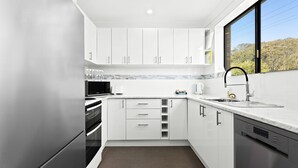 A modern kitchen with white cabinets, a built-in oven, a microwave, and a sink with a black faucet. - Apollo Unit 1 - Ground Floor - A Block (Narooma)