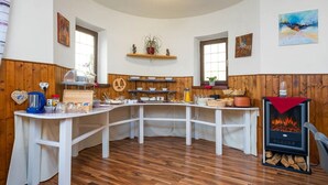 A cozy kitchen with wooden paneling, a central island, and a wood-burning stove. - Pension Bayerwald (Bodenmais)