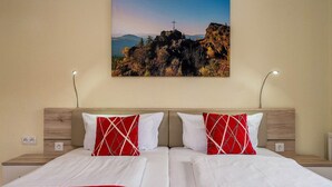 A double bed with white and red bedding, two bedside tables with lamps, and a wall-mounted picture of a mountain landscape. - Pension Bayerwald (Bodenmais)