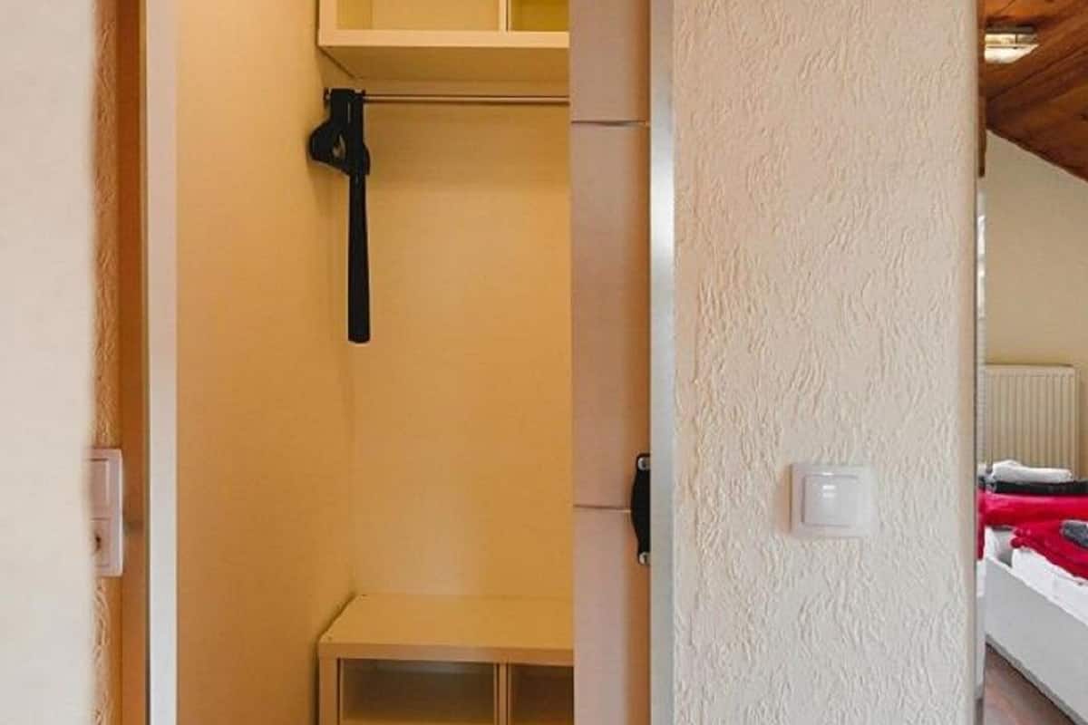 Un couloir étroit, doté d’un plancher en bois, mène à une pièce où se trouvent un lit et un miroir accroché au mur.