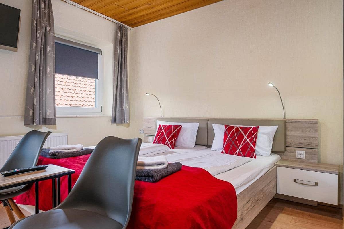 Une chambre d’hôtel comprenant un lit, deux tables de chevet, un bureau avec une chaise et une fenêtre avec des rideaux.