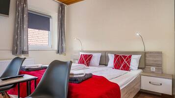 Habitación de hotel con cama, dos mesitas de noche, un escritorio con silla y una ventana con cortinas.