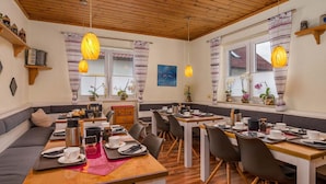 A cozy dining area with wooden tables and chairs, a sofa, and pendant lights. - Pension Bayerwald (Bodenmais)