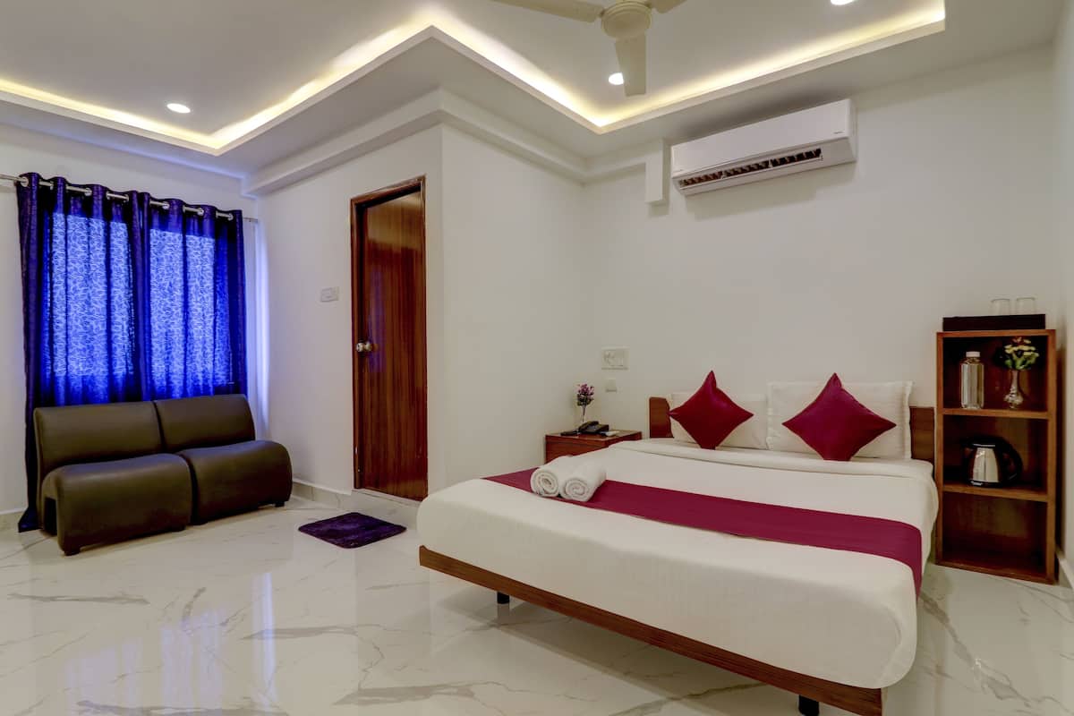 A modern hotel room with a large bed, a sofa, a nightstand, and a shelf with decorative items.