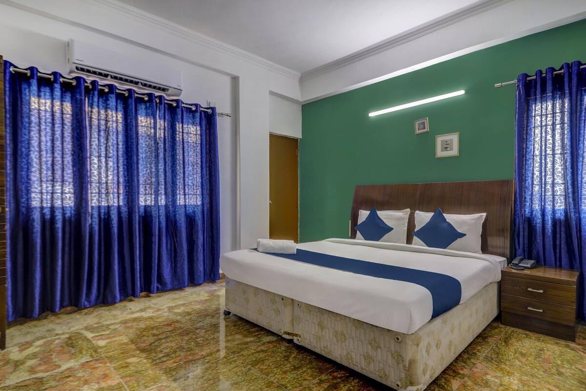 A hotel room with a bed, a wooden nightstand, a green accent wall, and blue curtains.