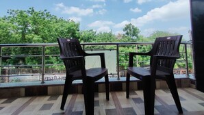 A balcony with two chairs and a table, overlooking a green landscape with trees and a clear sky. - Hilltop Residency (Sawai Madhopur)