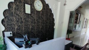 A reception desk with a clock, a small Buddha statue, and a chair. - Hilltop Residency (Sawai Madhopur)
