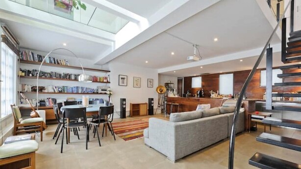 A spacious living area with a dining table, chairs, a sofa, a staircase, and a kitchen area. - Loft Style Apartment (London)