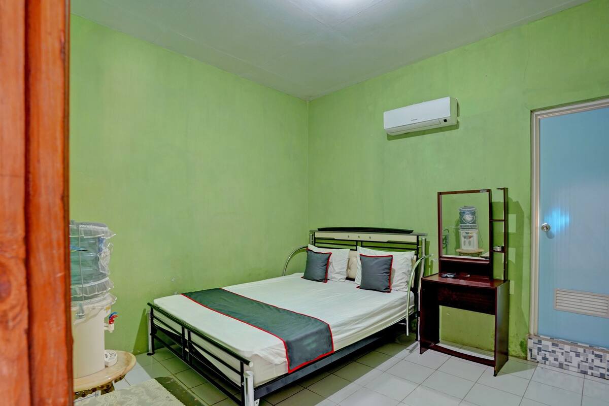 A room with a bed, a bedside table, a water dispenser, and a mirror.