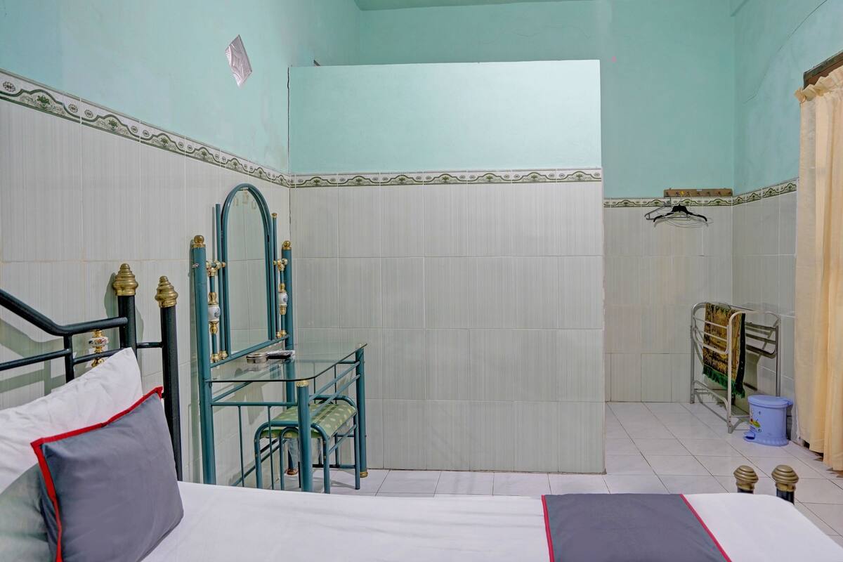A hotel room with a bed, a small table with chairs, a mirror, and a shower area.