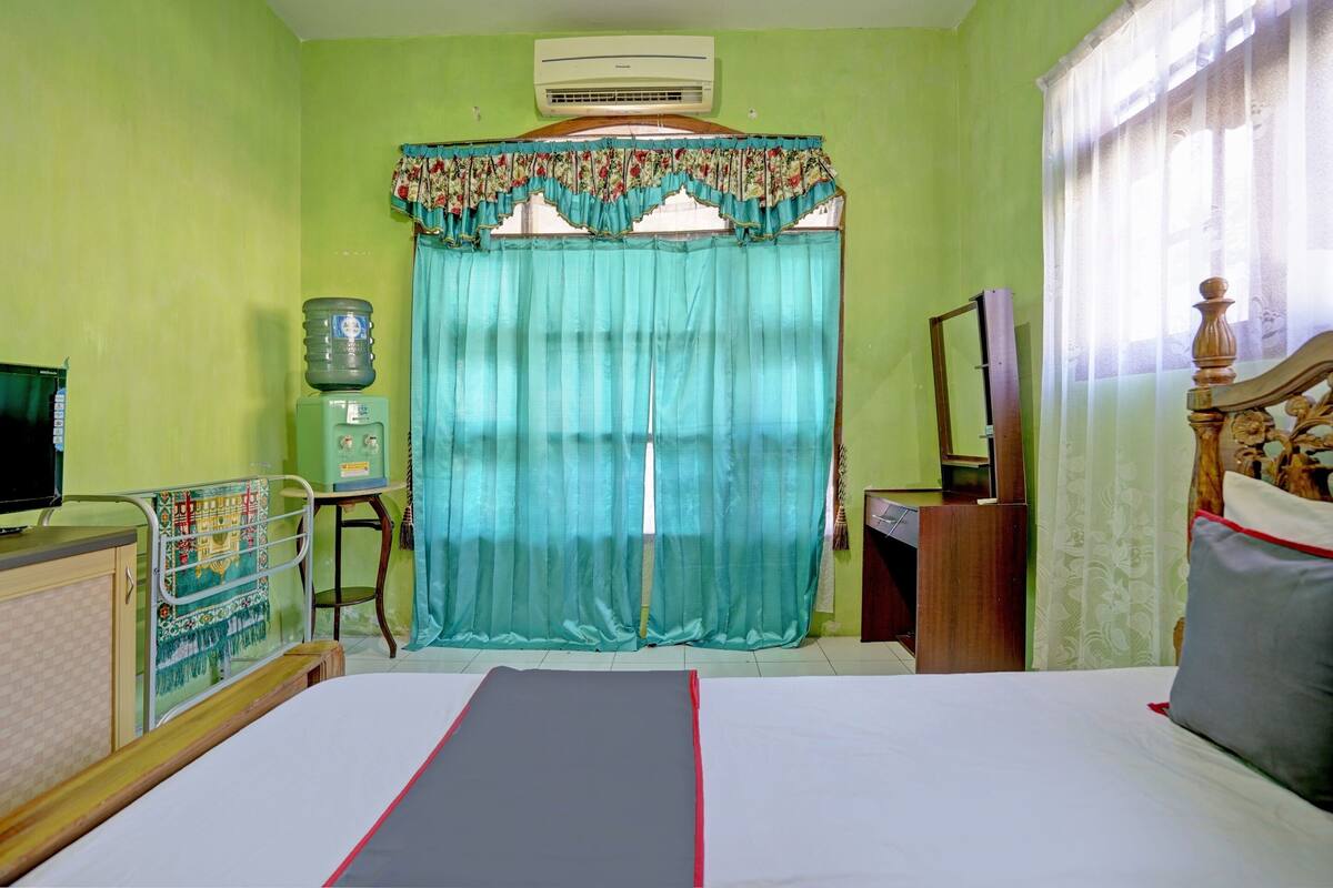 A room with a bed, a water dispenser, a television, and a window with curtains.