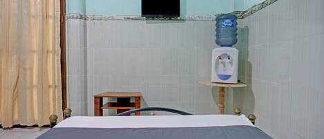 A hotel room with a bed, a water dispenser, a television mounted on the wall, and a curtain.