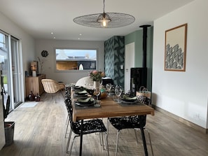 Zona pranzo con tavolo in legno apparecchiato per quattro persone, circondata da sedie nere, una lampada a sospensione e vista sull'esterno.