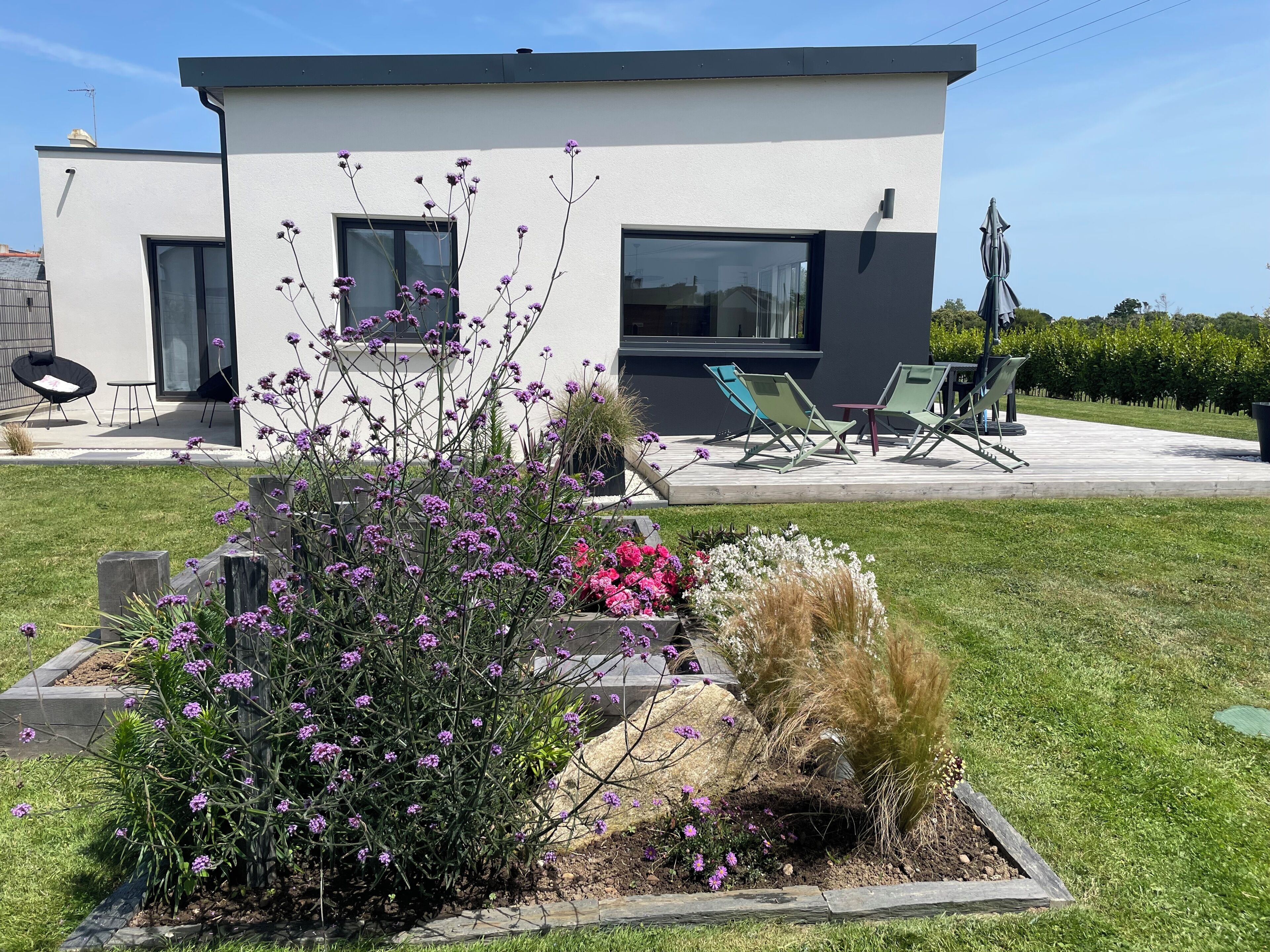 Una casa moderna con un patio amueblado y un jardín lleno de plantas y flores.