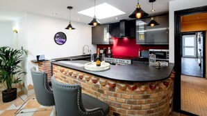 A modern kitchen with a central island, black chairs, and pendant lighting. - Spa Retreat (relaxation centre) (Portsmouth)