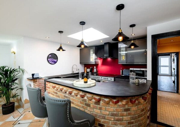 A modern kitchen with a central island, black chairs, and pendant lighting.