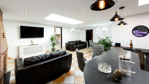 A modern living room with a black sofa, a dining table with chairs, and a TV mounted on the wall. - Spa Retreat (relaxation centre) (Portsmouth)