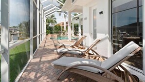 A covered outdoor area with lounge chairs and a pool. - Waterfront 3BR/3BA Marco Island home with heated pool and free WiFi. (Marco Island)