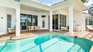 A pool area with a clear blue pool, sun loungers, and a covered patio with chairs and tables. - Waterfront 3BR/3BA Marco Island home with heated pool and free WiFi. (Marco Island)