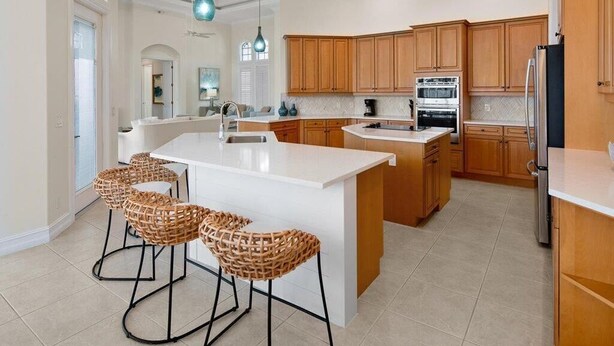 A modern kitchen with a central island, wooden cabinets, and hanging pendant lights. - Waterfront 3BR/3BA Marco Island home with heated pool and free WiFi. (Marco Island)
