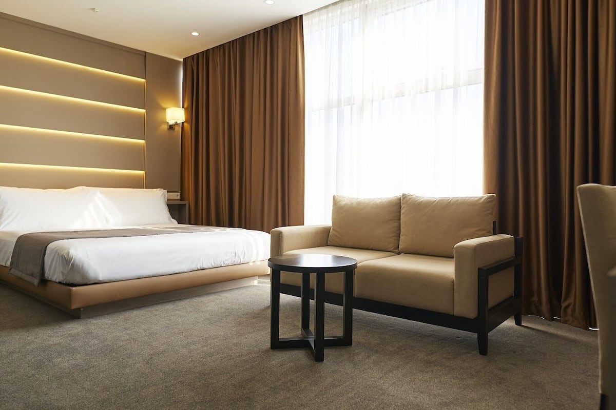 A hotel room with a bed, a sofa, a small table, and a lamp.