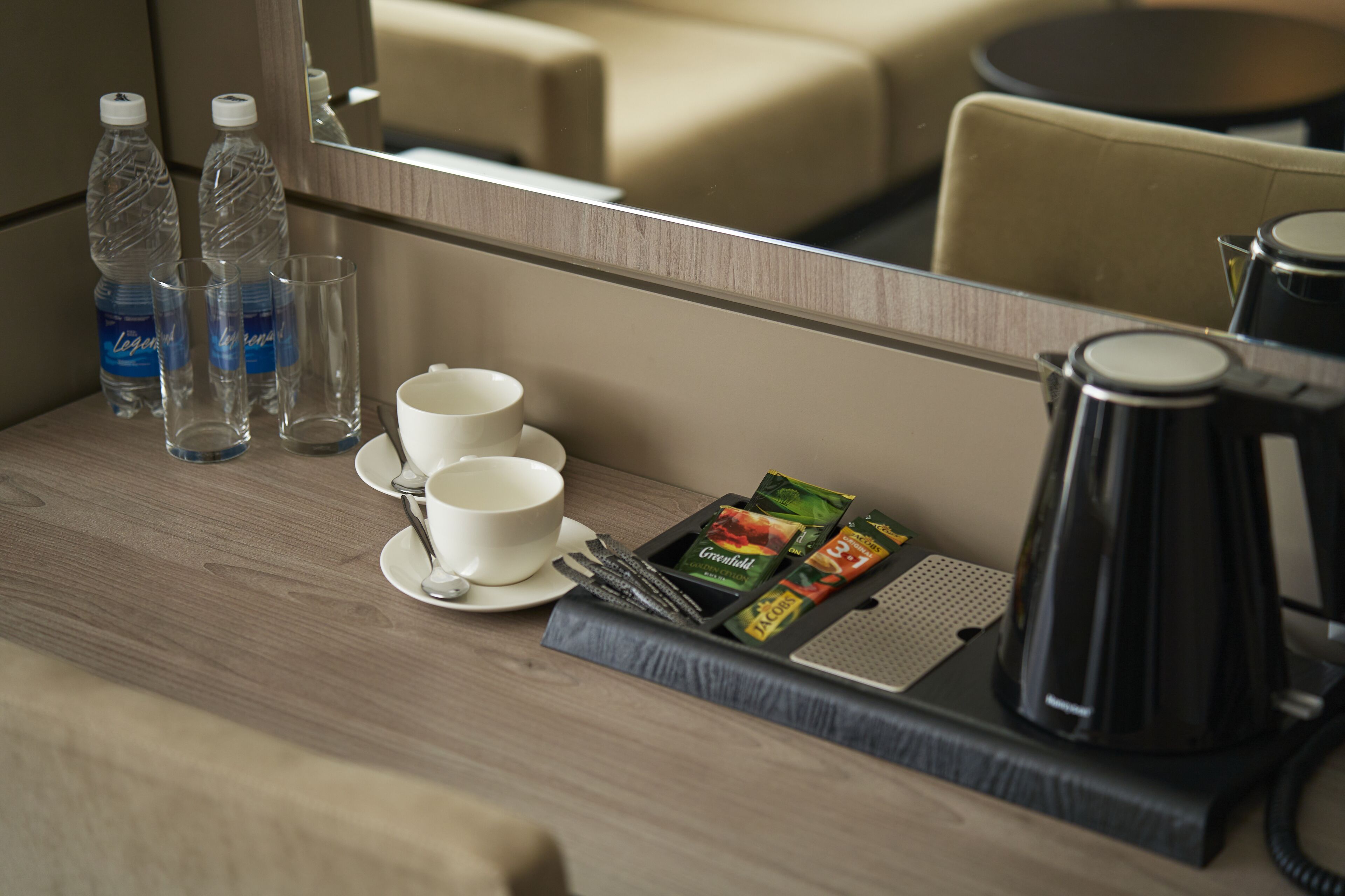A hotel room's minibar with bottled water, glasses, cups, and a tray of snacks.