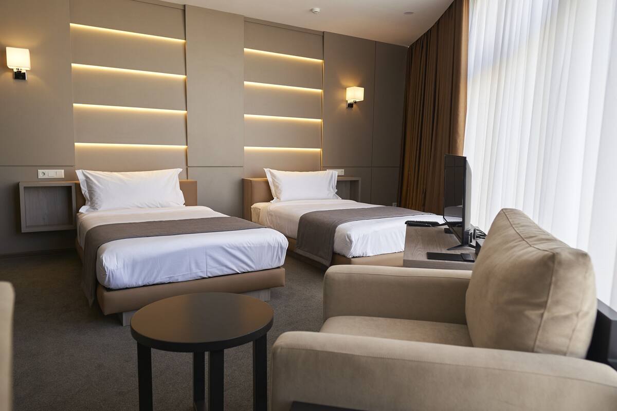 A hotel room with two beds, a sofa, a small table, and a TV.