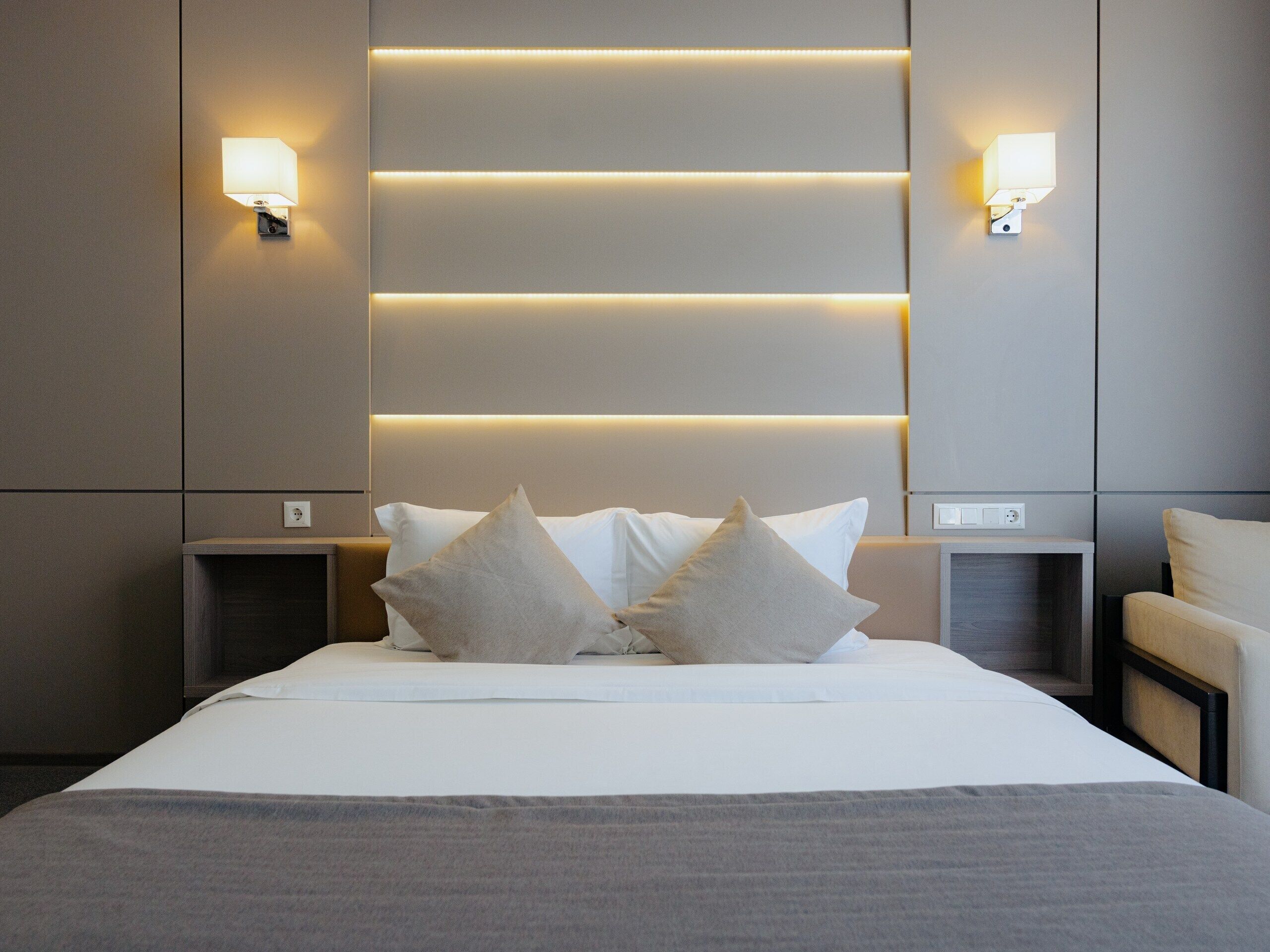 A modern hotel room with a large bed, two bedside tables, and wall-mounted lighting.