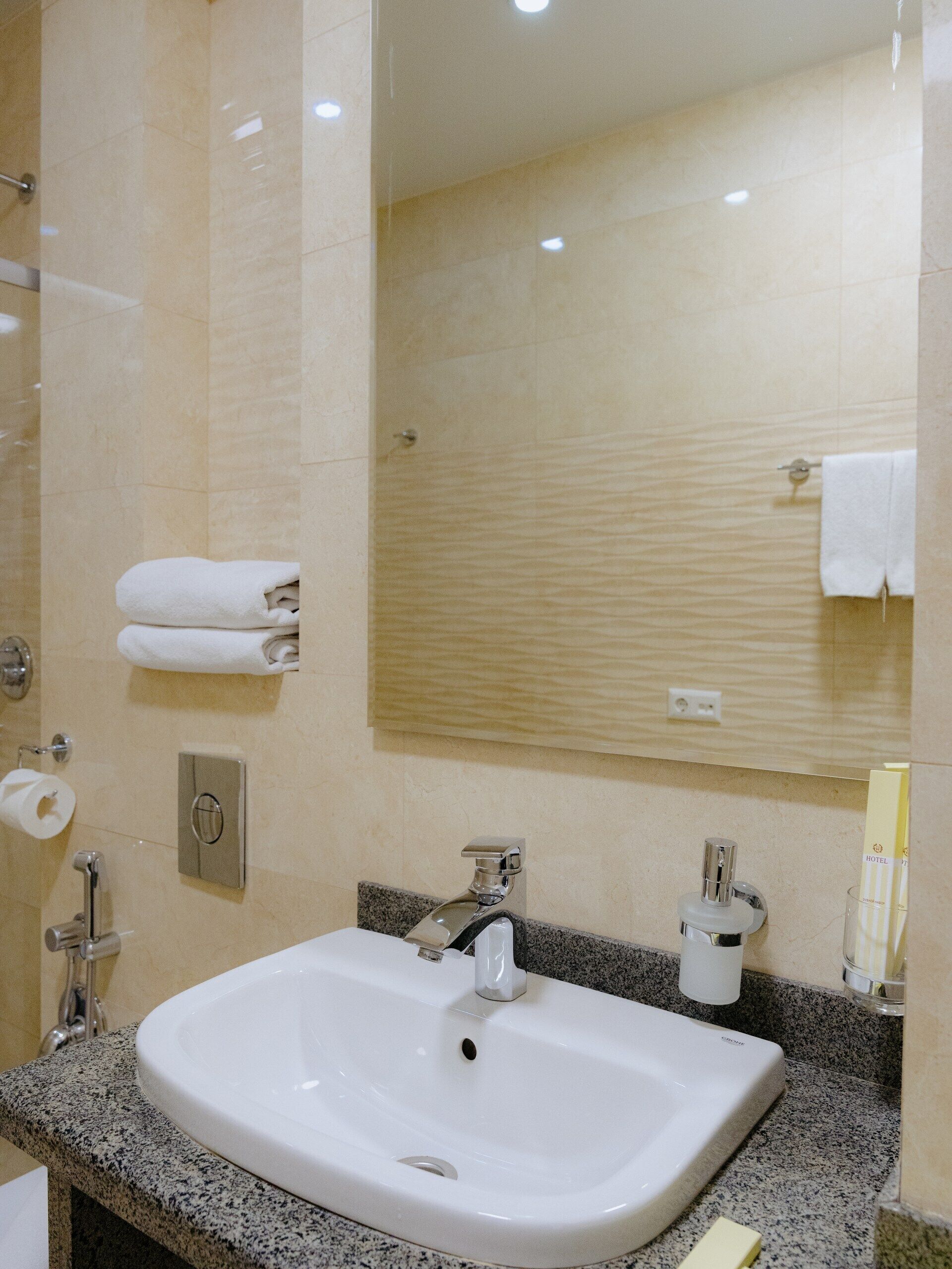 A bathroom with a white sink, a mirror, a towel rack, and a toilet paper holder.