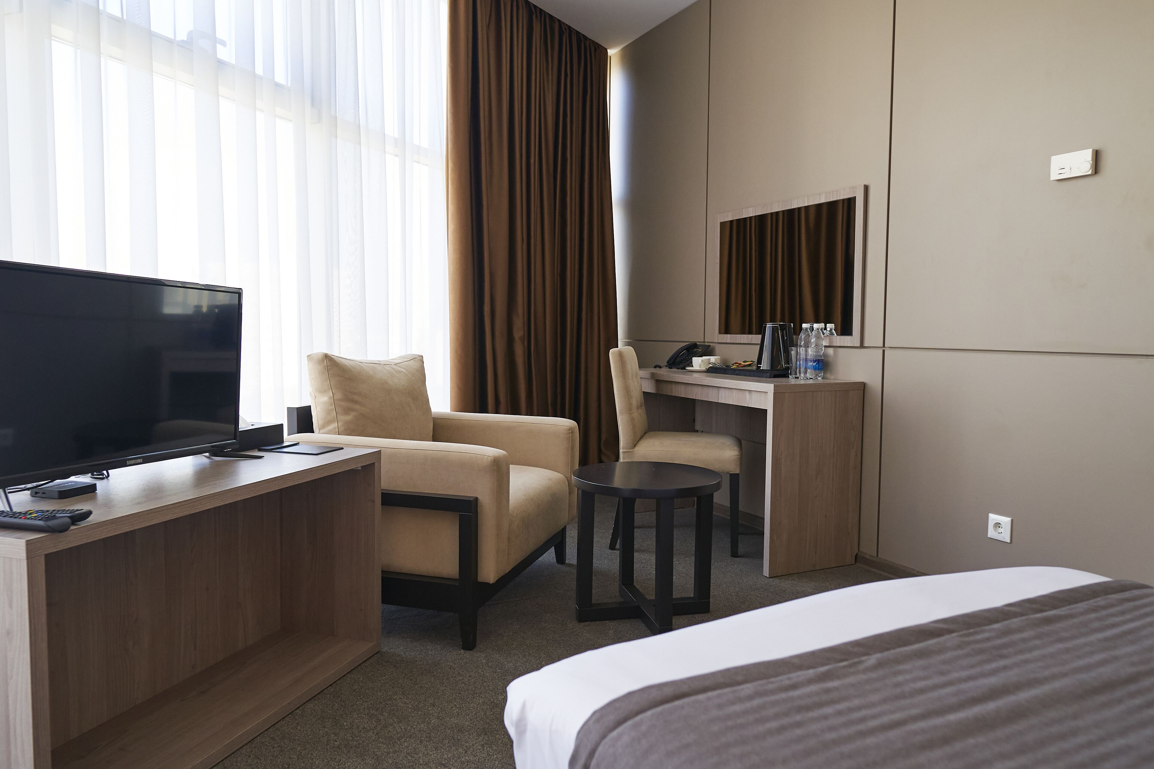 A hotel room with a bed, a desk with a computer, a TV, and a chair.