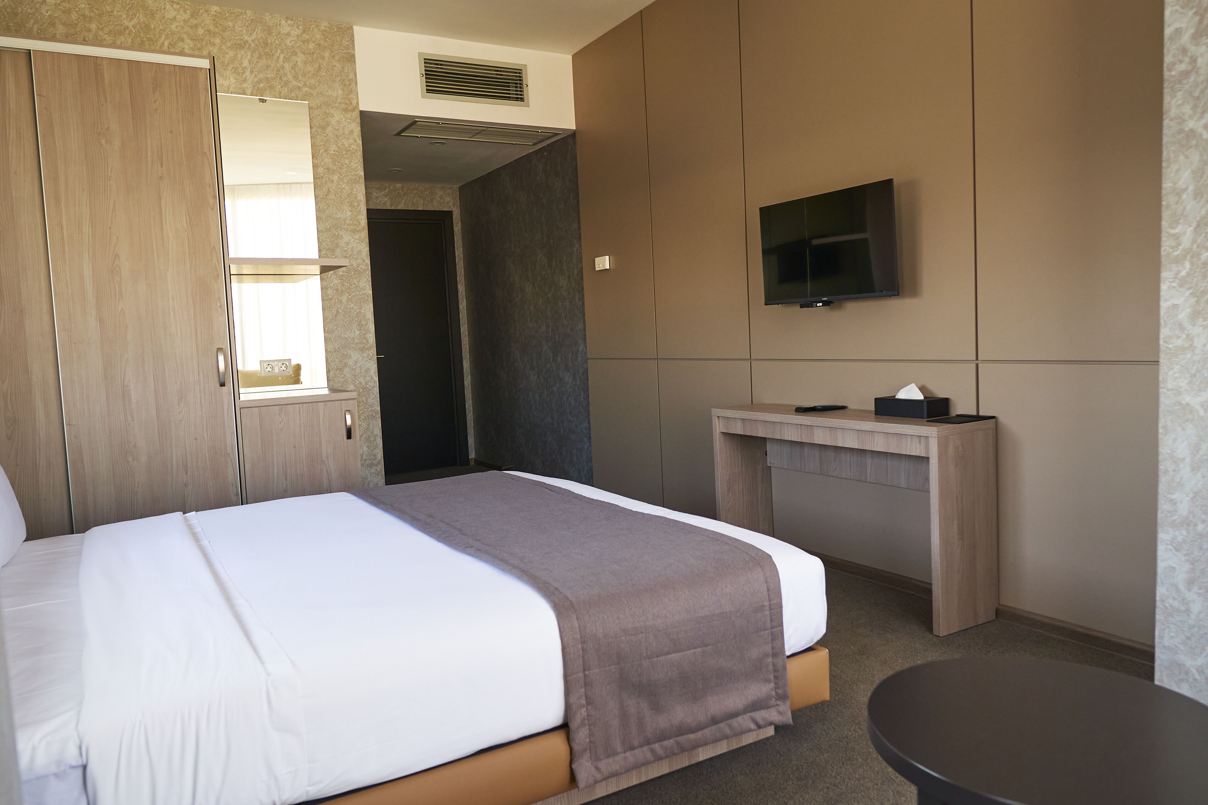 A hotel room with a bed, a desk, a TV, and a wardrobe.