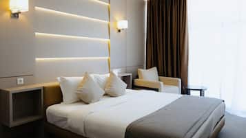 A modern hotel room with a large bed, bedside tables, a chair, and a large window with curtains.