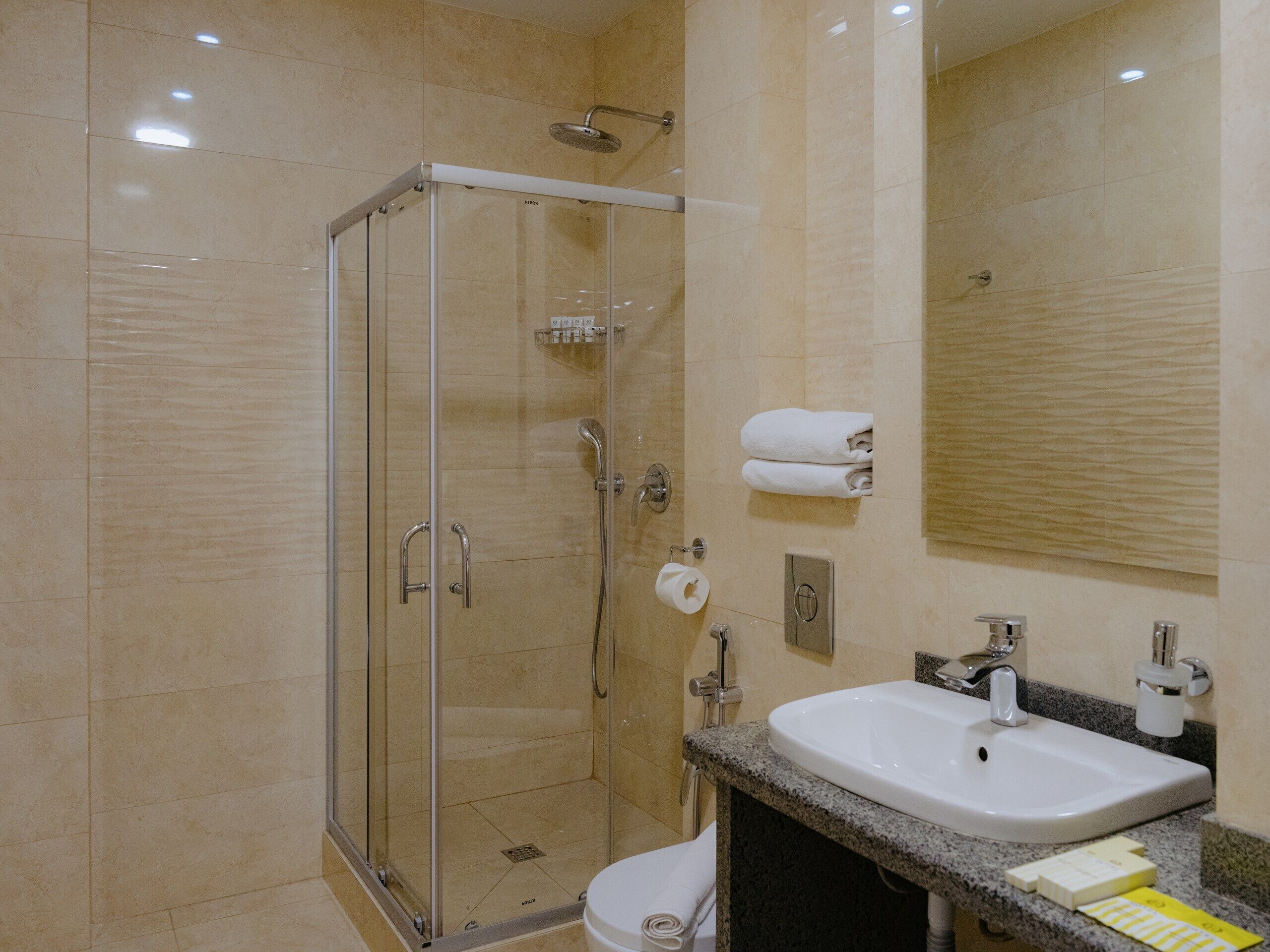 A hotel bathroom with a glass-enclosed shower, a sink, and a mirror.