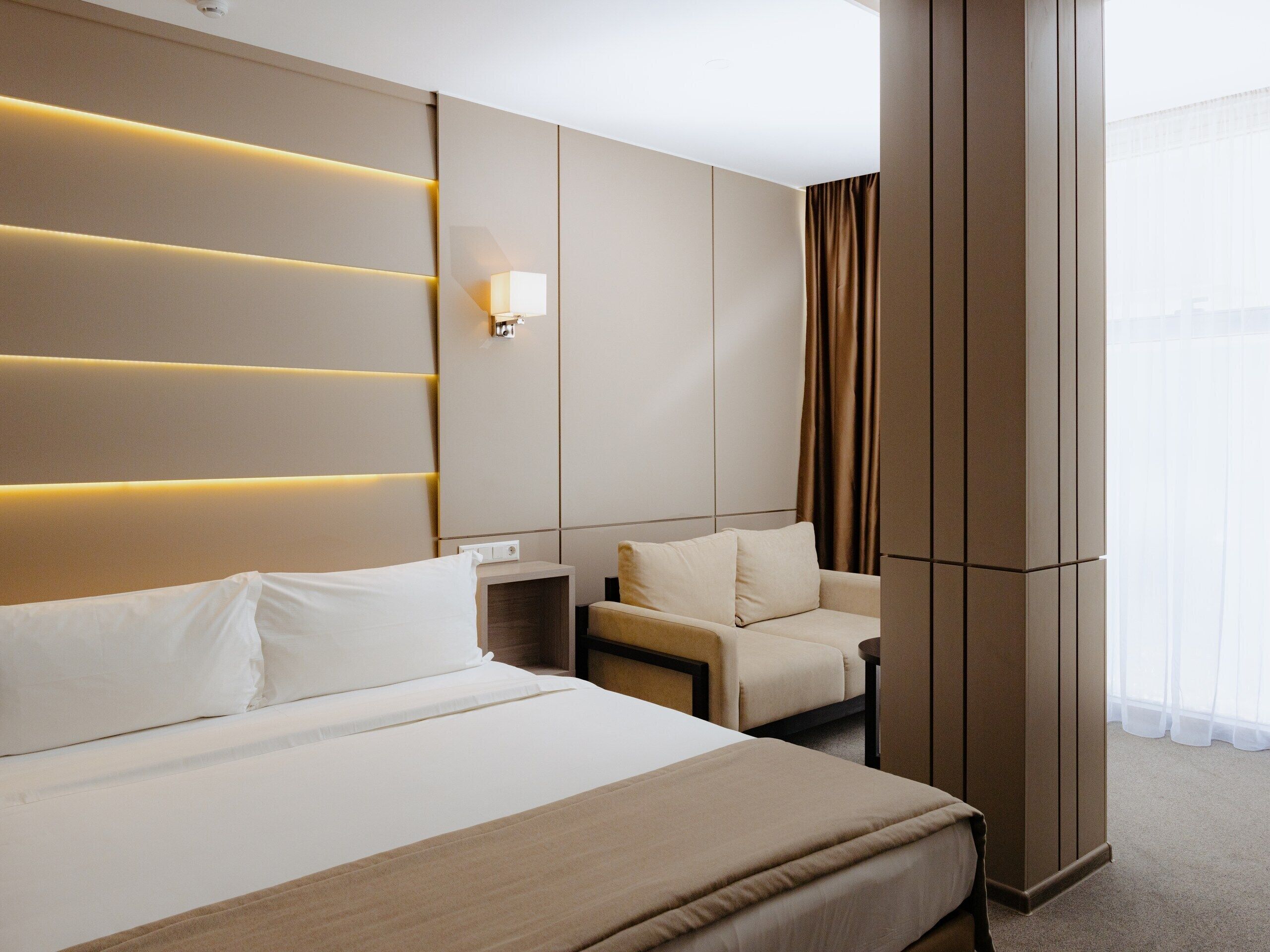 A hotel room with a large bed, a bedside table, a chair, and a wall-mounted light fixture.