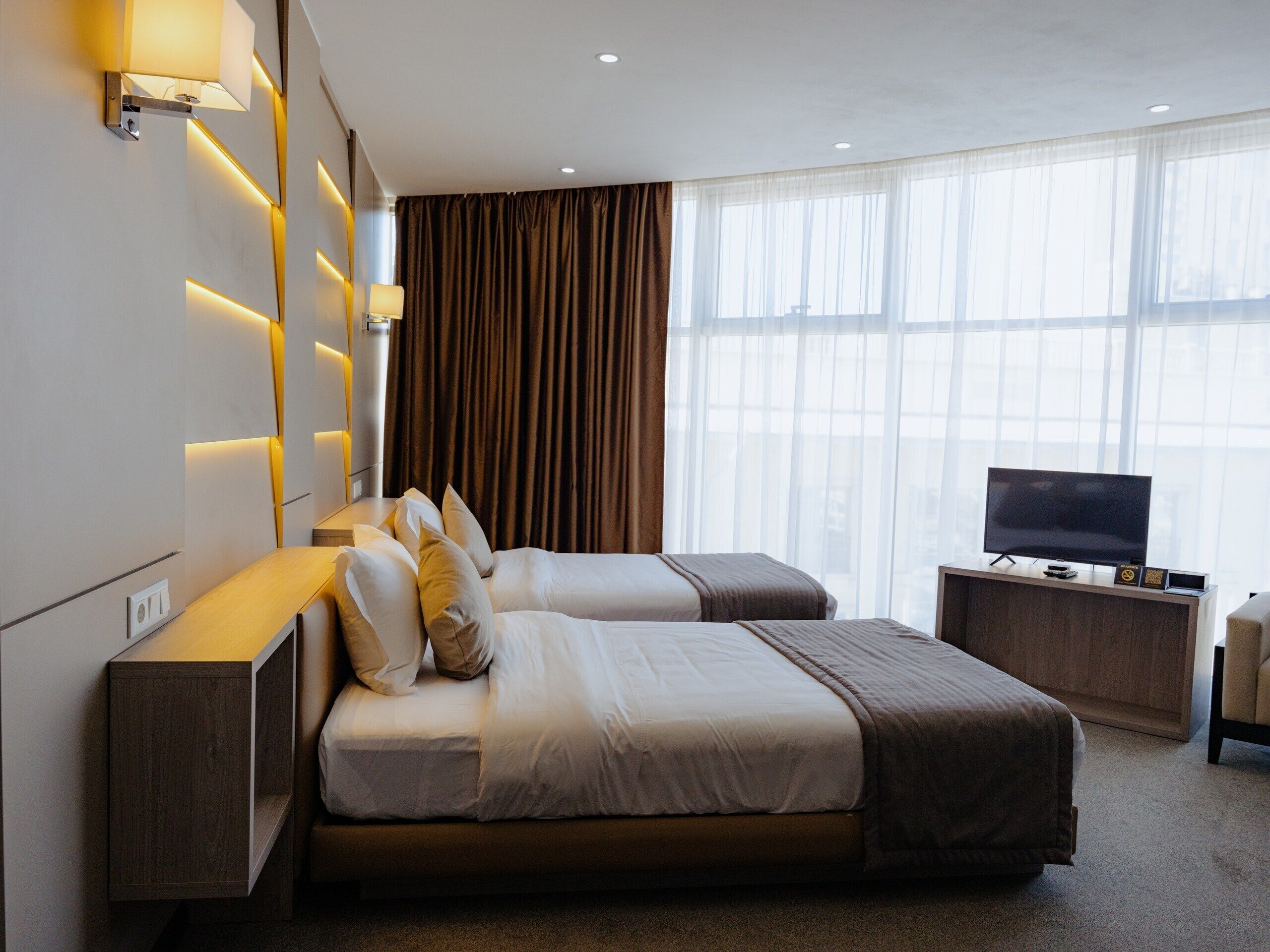 A modern hotel room with two beds, a TV, and a desk.