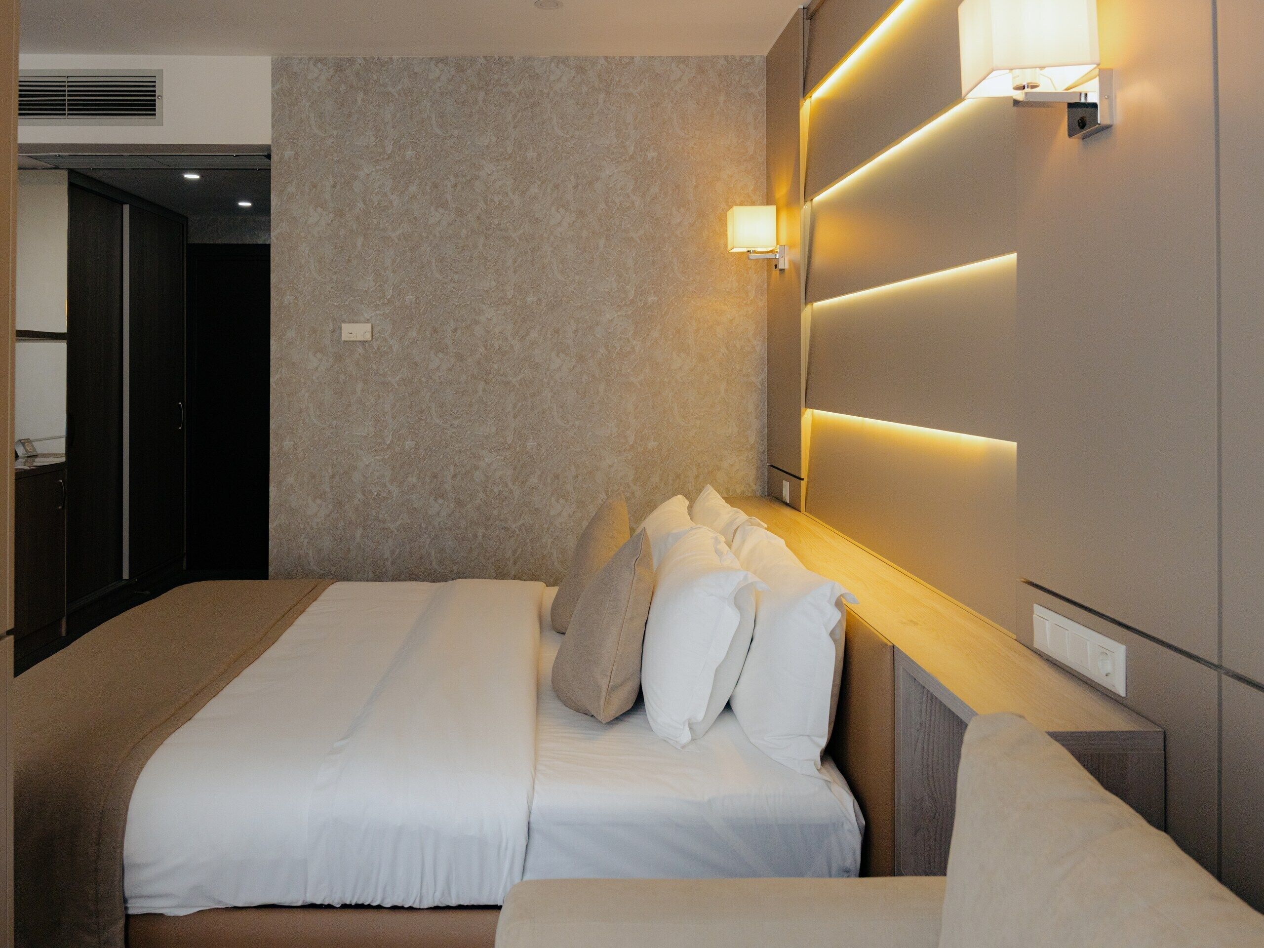 Habitación de hotel con una cama grande, una mesita de noche, una lámpara de pared y una puerta que da a un armario.