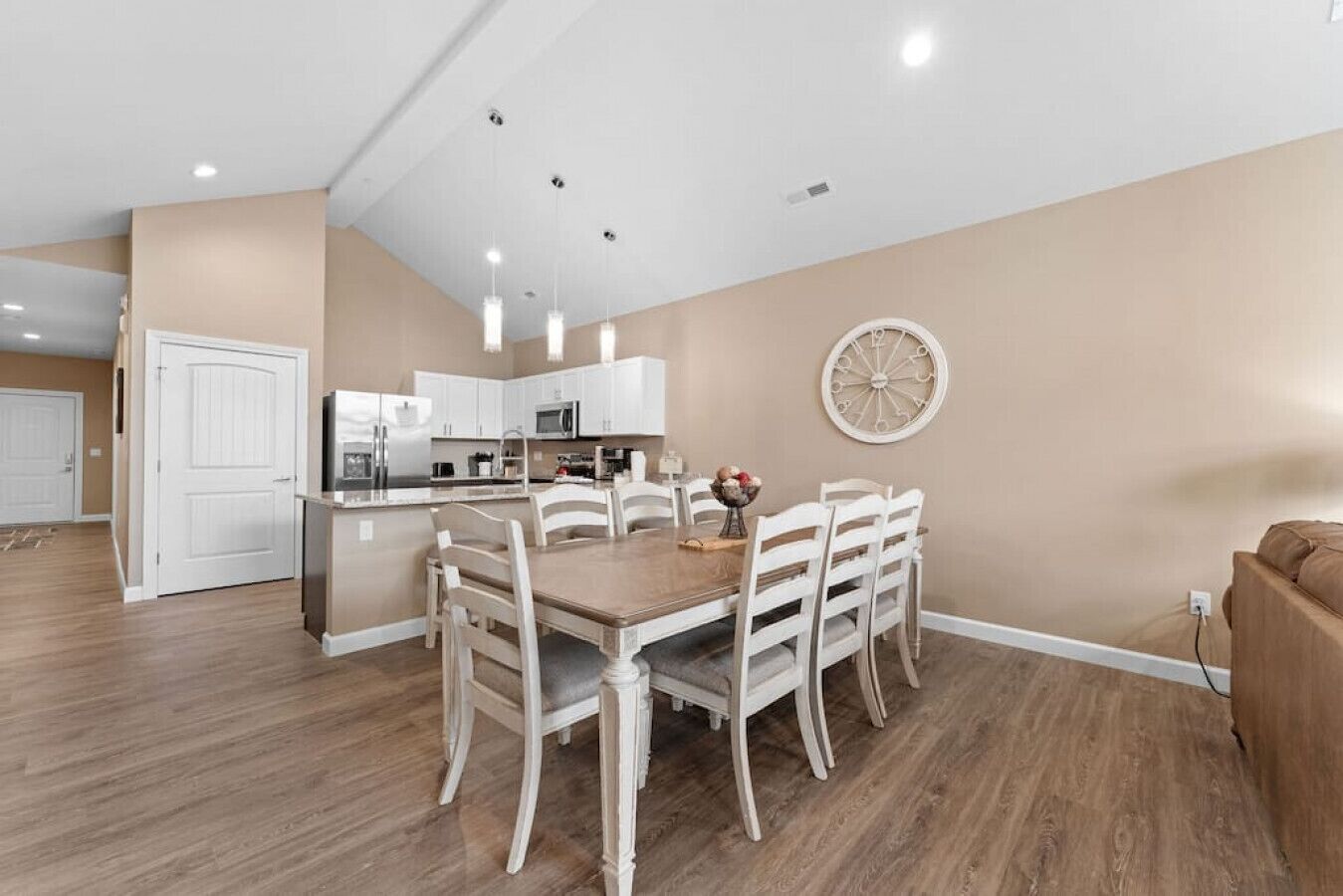 A modern kitchen with white cabinets, a dining area with a wooden table and white chairs, and a large decorative wall clock.