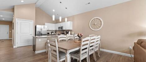 A modern kitchen with white cabinets, a dining area with a wooden table and white chairs, and a large decorative wall clock.
