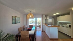 A modern kitchen with white cabinets, a dining area with wicker chairs, and a large window.