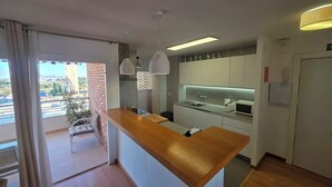 A modern kitchen with a wooden island, pendant lights, and a view of the city through a balcony.