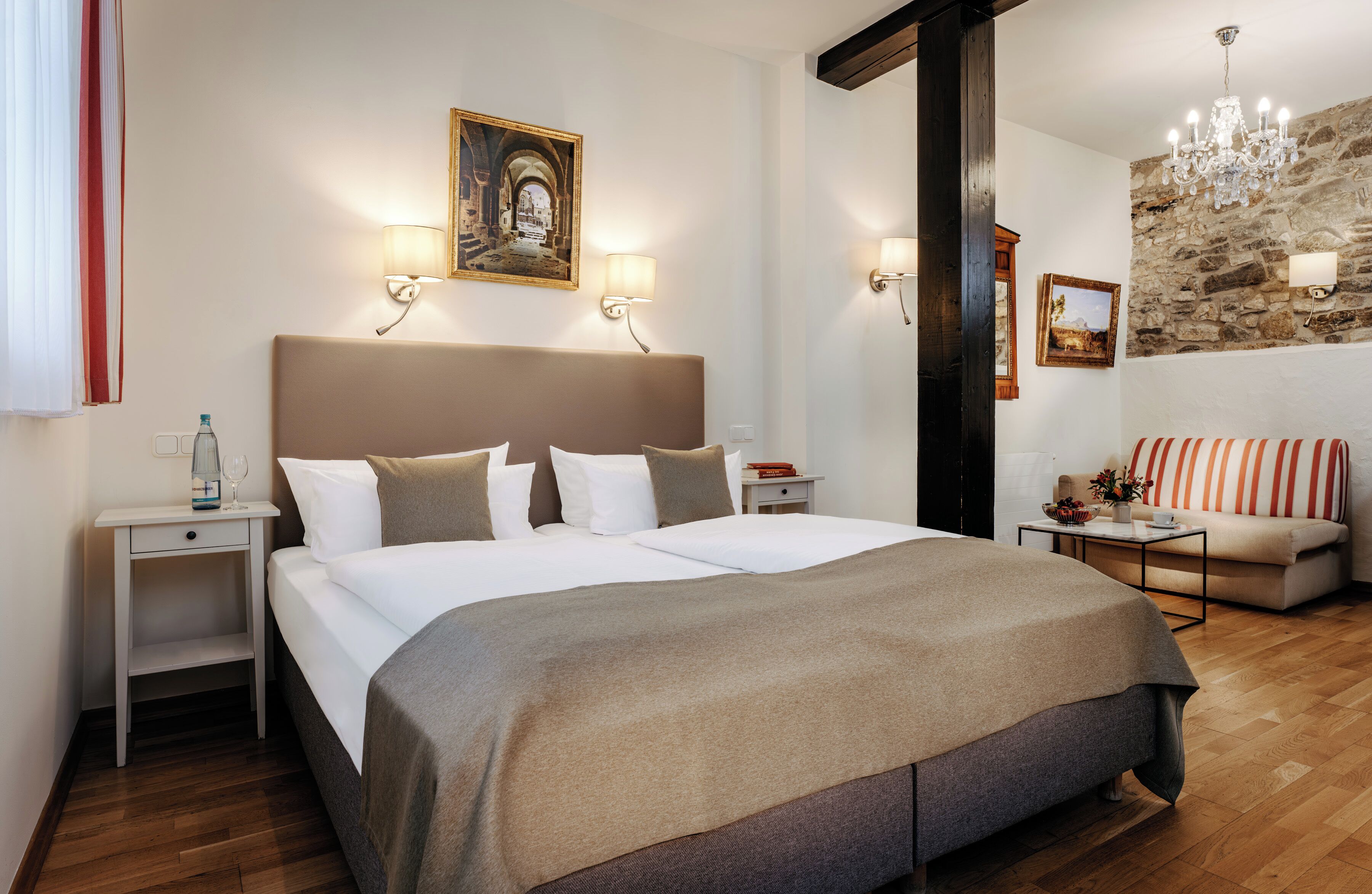 Hotellihuone, jossa on suuri sänky, kaksi yöpöytää, yölamppu, sohva, kattokruunu ja kiviseinä.
