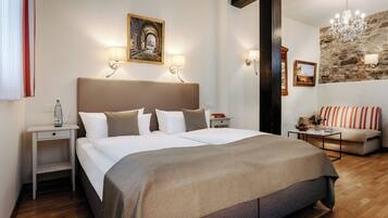 Quarto de hotel com uma cama grande, duas mesas de cabeceira, um criado-mudo, um sofá, um candelabro e uma parede de pedra.