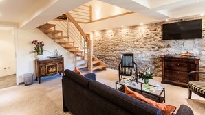 A spacious living area with a stone wall, a wooden staircase, a flat-screen TV, and a dining table set with a vase of flowers. - Romantik Hotel Alte Münze (Goslar)