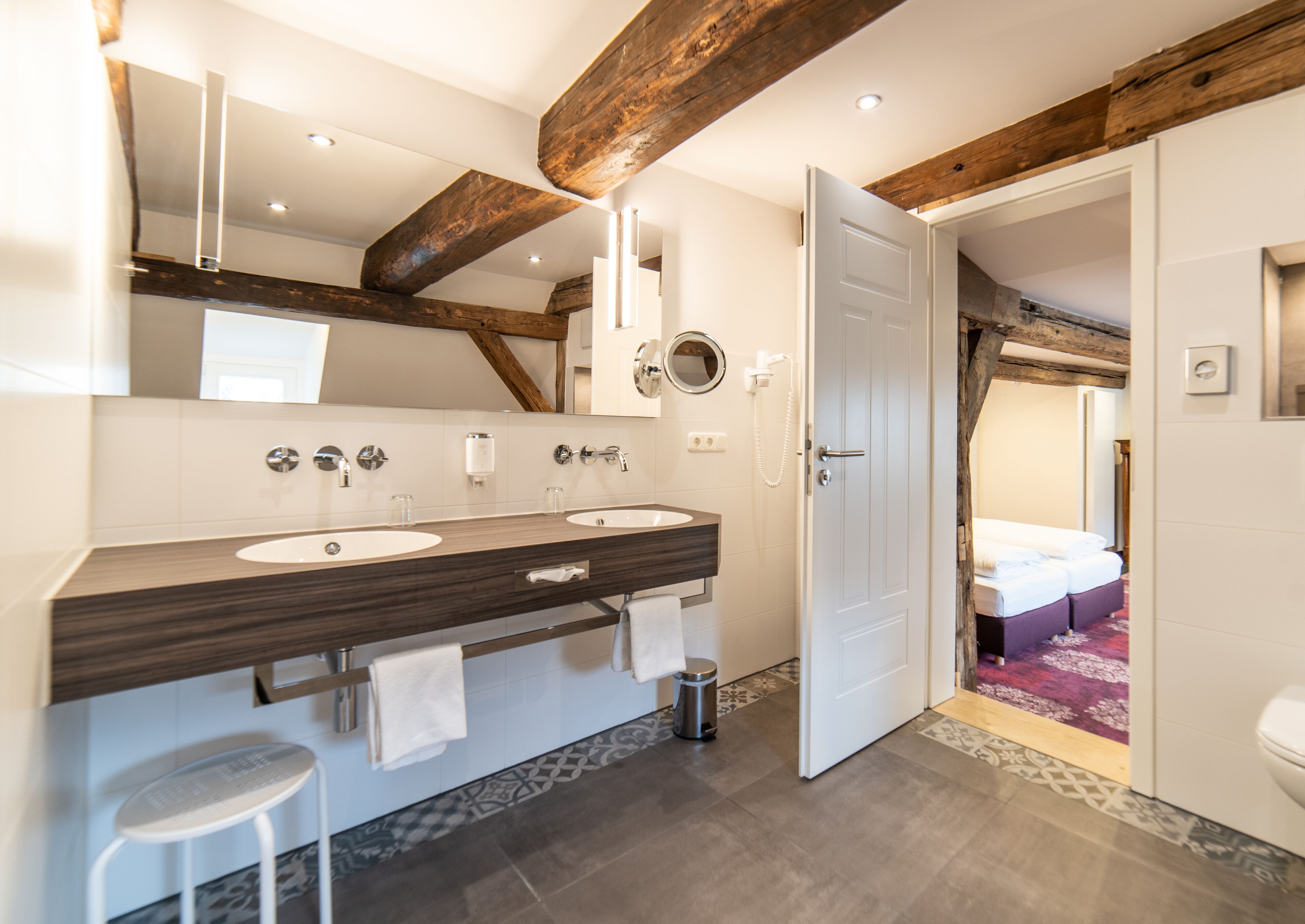 Une salle de bain moderne avec deux vasques, un grand miroir et des poutres en bois au plafond.